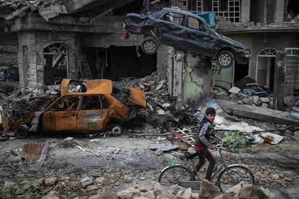 A boy rides his bike past destroyed cars and houses in a neighborhood recently liberated by Iraqi security forces on the western side of Mosul on March 19, 2017. (AP)